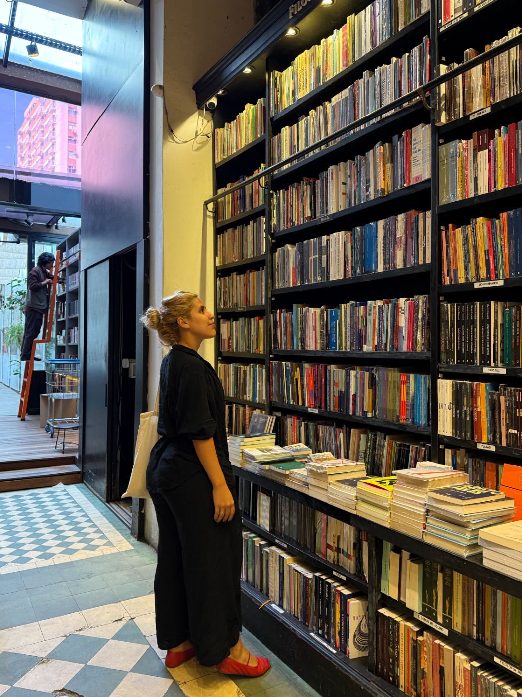 Maria Marta em uma livraria, diante da estante de filosofia